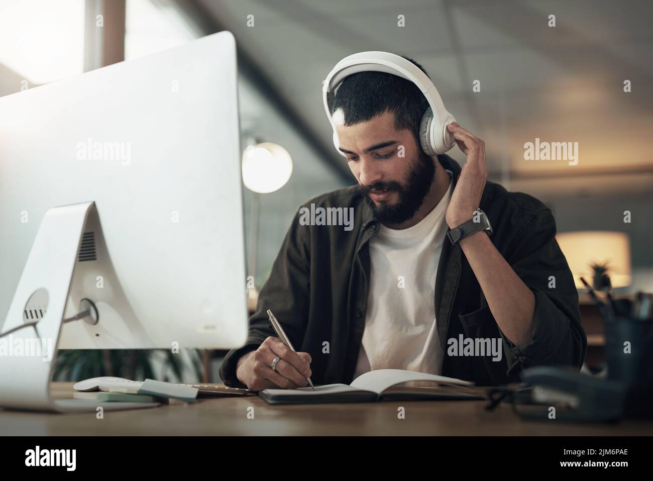 Gute Musik hält die kreativen Säfte fließen. Ein junger Geschäftsmann in einem Notebook schreiben und mit einem Computer mit Kopfhörern während eines späten Nachts Stockfoto