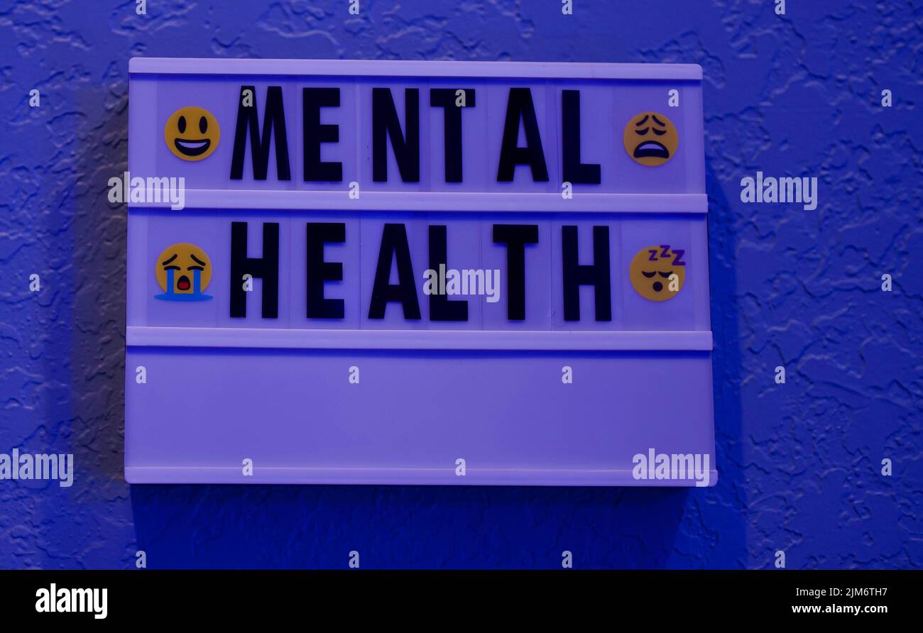 Ein weißes Schild mit den Worten „mentale Gesundheit“ und 4 Emojis mit unterschiedlichen Emotionen Stockfoto