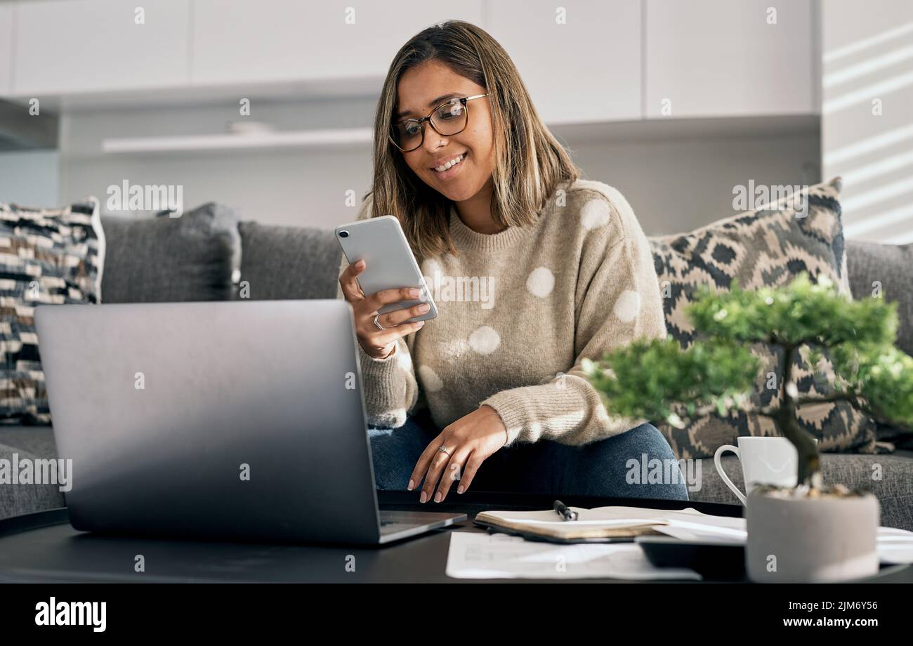 Meine Kollegen und ich nutzen Online-Nachrichten, um einander auf dem Laufenden zu halten. Eine Frau, die ihr Handy und ihren Laptop benutzt, während sie von zu Hause aus arbeitet. Stockfoto