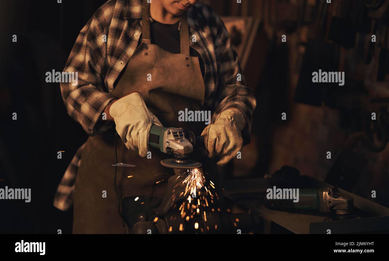 Frauen sind stärker als Stahl. Eine Frau, die einen Winkelschleifer benutzt, während sie in einer Gießerei arbeitet. Stockfoto