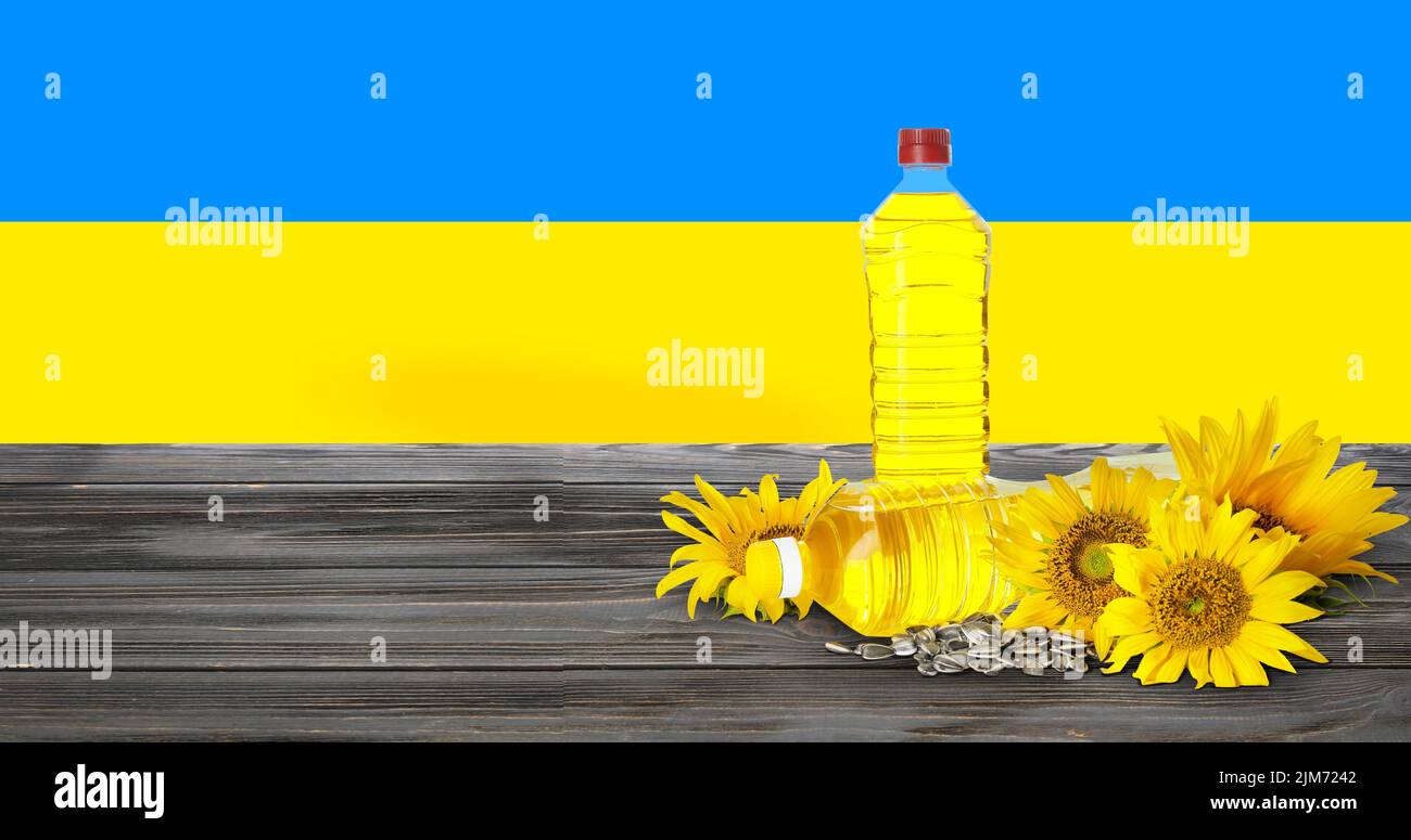 Flaschen Sonnenblumenöl und Samen auf Holztisch gegen die Flagge der Ukraine Stockfoto