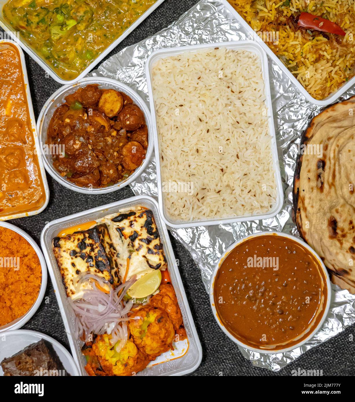 Draufsicht auf eine Vielzahl von indischen Speisen zum Mitnehmen in weißen Kunststoffbehältern auf einem Stoffhintergrund. Stockfoto