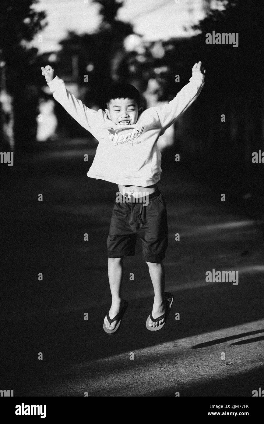 Eine vertikale Graustufenaufnahme eines Kindes, das fröhlich auf und ab springt Stockfoto