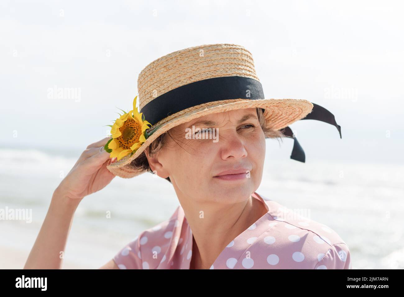 Frau in einem rosa Kleid mit weißen Tupfen und einem Bootsfahrer mit Sonnenblume, nachdenklich wegblickend, auf einem verschwommenen Meeresgrund. Stockfoto