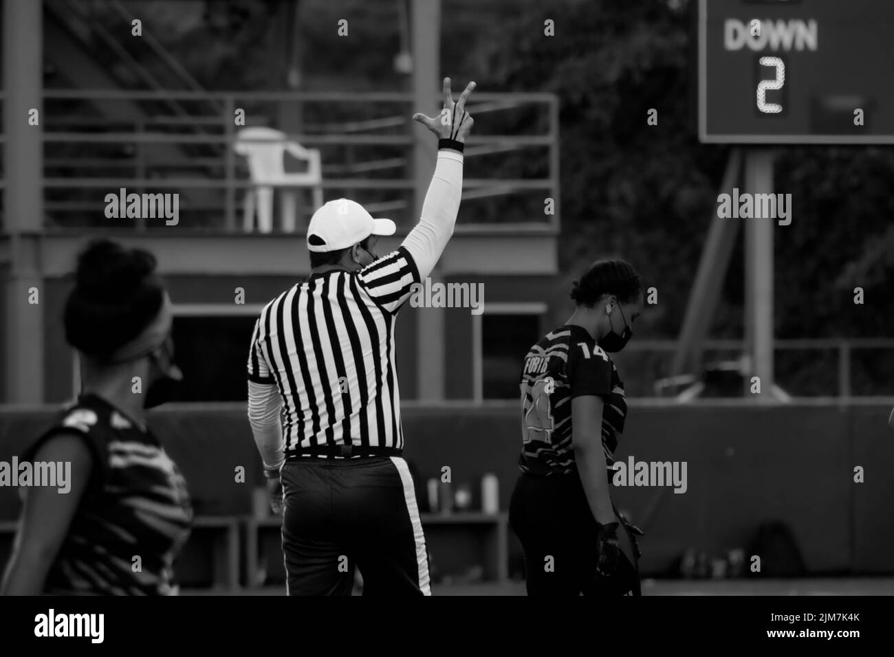 Eine Graustufenaufnahme eines männlichen Schiedsrichters, der während eines Flag-Fußballspiels auf dem grünen Feld ein Faustzeichen tut Stockfoto