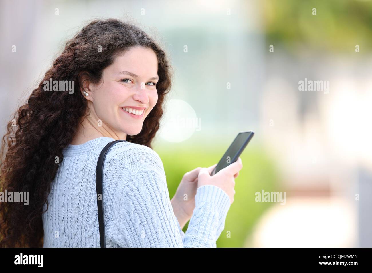 Glückliche Frau, die Smartphone benutzt, die auf der Straße herumläuft und einen anschaut Stockfoto