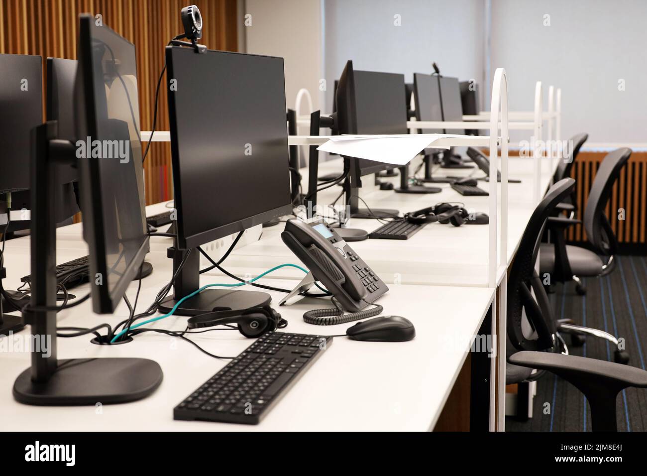 Bürofläche mit PC-Monitoren, Telefonen und Headsets auf den Tischen. Coworking-Bereich, leeres Call Center, Firmengeschäft Stockfoto