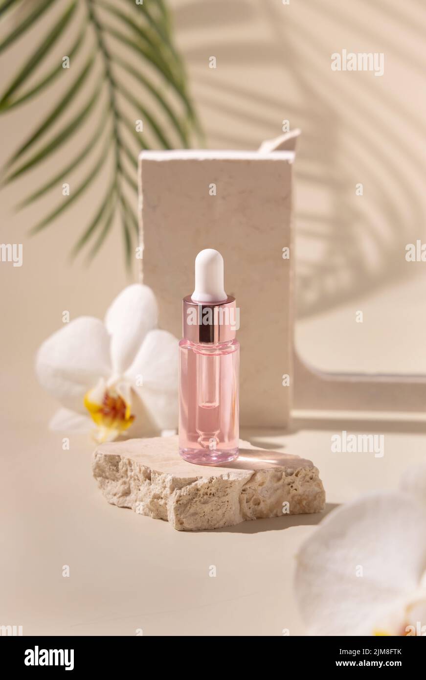 Tropfflasche auf Stein in der Nähe von weißen Orchideenblüten und Palmenblättern auf hellgelb, Nahaufnahme, Mockup. Hautpflegeprodukt, ätherisches Öl oder Serum. Stockfoto