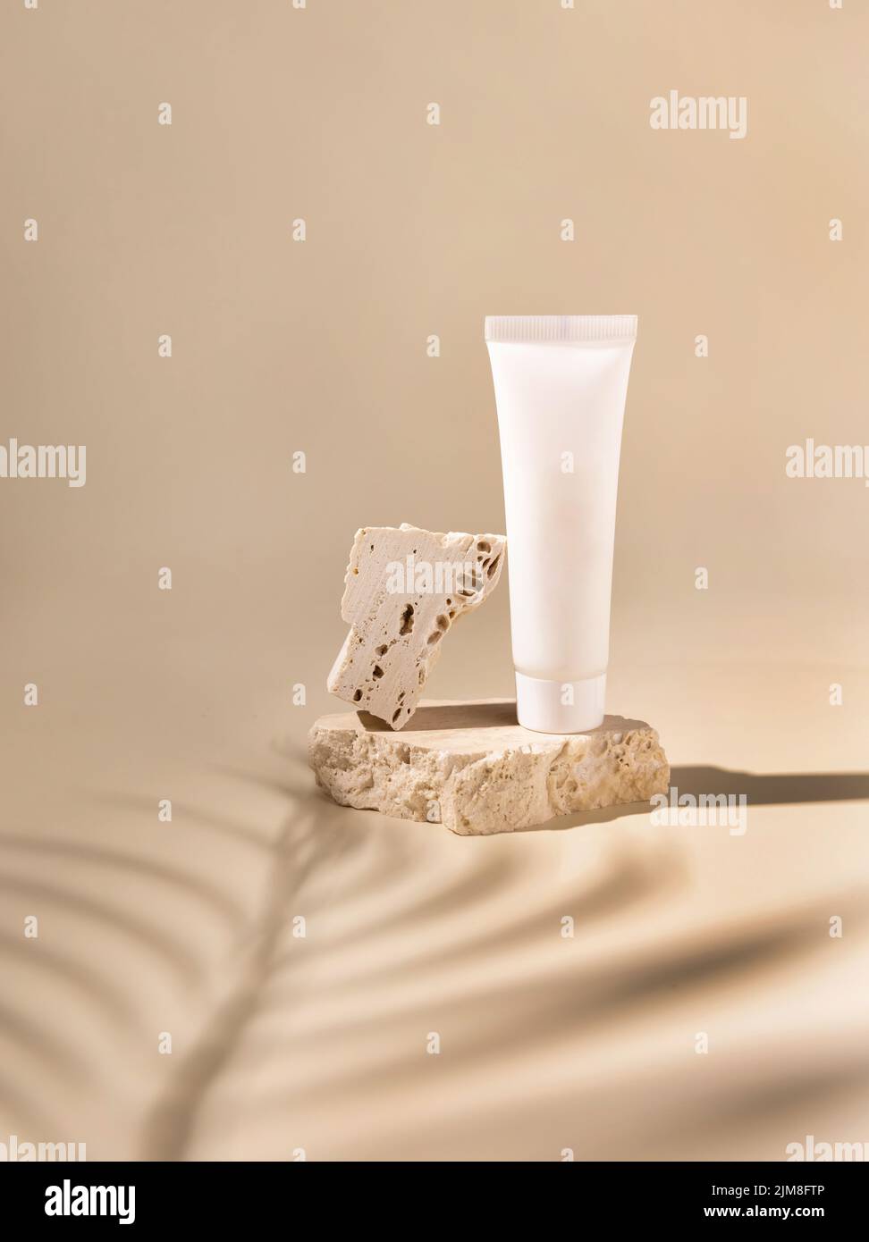 Weißes cremefarbenes Plastikröhrchen auf Travertin-Stein auf hellgelb, harte Schatten von Palmblättern, Nahaufnahme, Nachbildung. Hautpflegeprodukt. Naturkosmetik. Bo Stockfoto