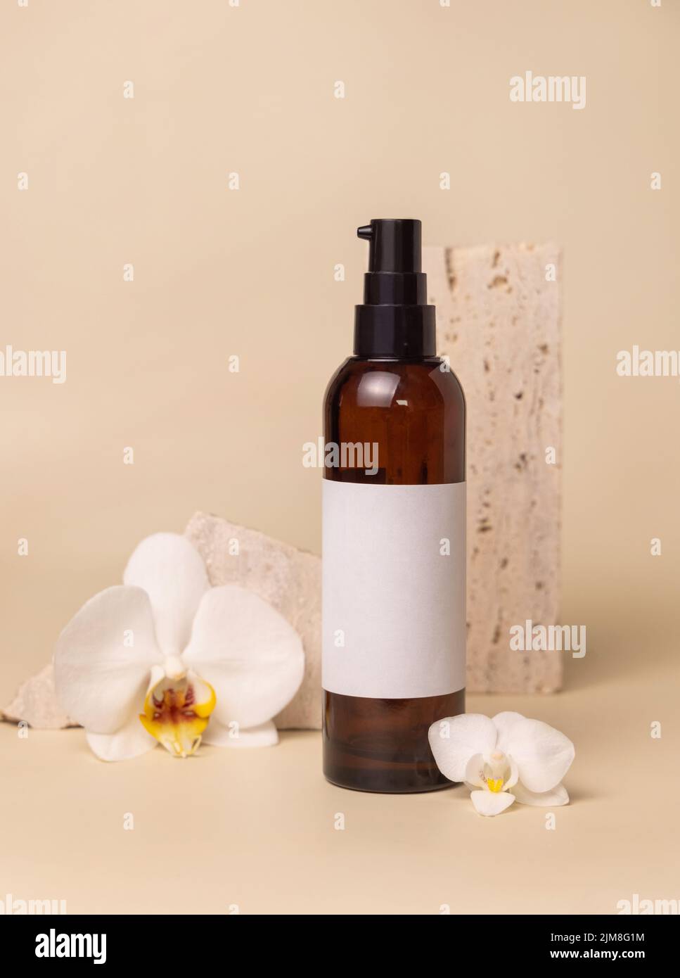 Dunkle Glas-Kosmetikflasche mit leerem Etikett in der Nähe von weißen Orchideenblumen und Steinen auf hellgelb, Nahaufnahme, Mockup. Hautpflege handgemachtes Beauty-Produkt, Stockfoto