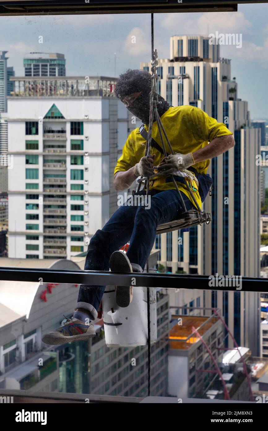 Thailändischer Arbeiter repariert Fenster in Hochhausgebäude mit Seil und Riemenscheibe, Bangkok, Thailand Stockfoto