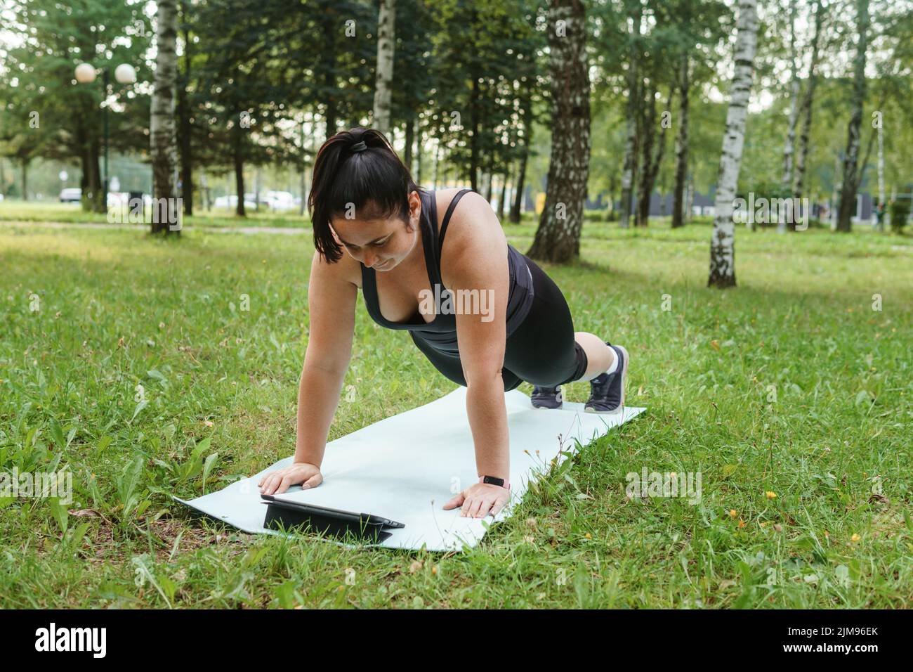 Eine charmante Brünette Frau plus-Größe Körper positiv praktiziert Sport in der Natur. Frau macht Yoga im Park auf einer Sportmatte. Auf einer Yogamatte im Hundepo Stockfoto