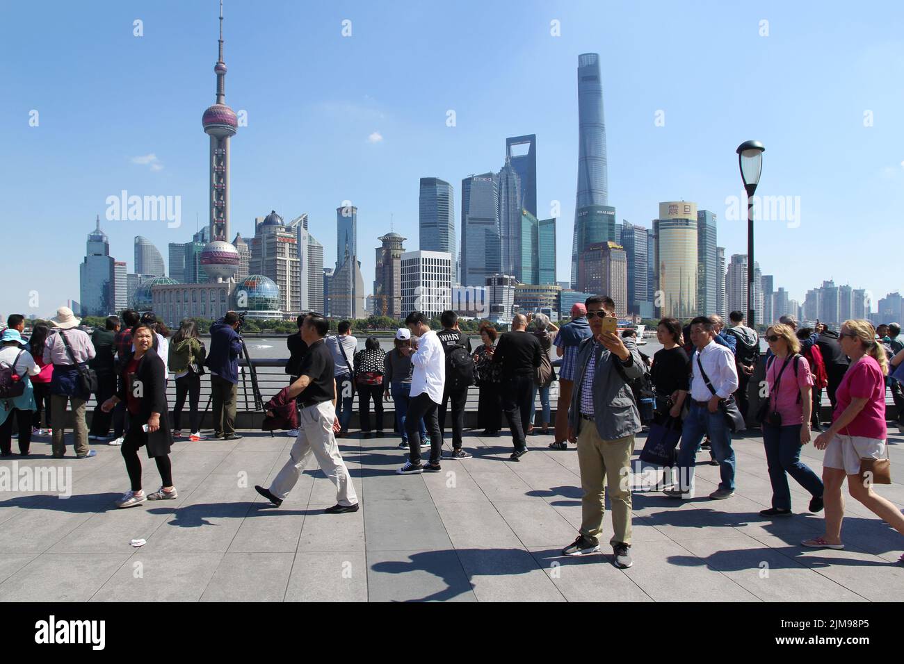 Touristenmassen, die am Bund vorbei spazieren und Fotos von Shanghais klassischer Skyline machen - dem Geschäftsviertel Pudong (China). Stockfoto