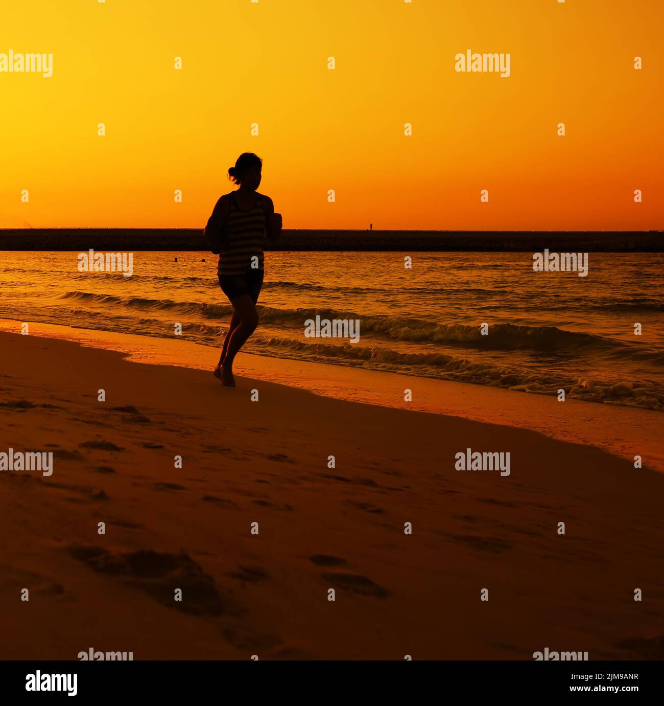 Frau joggt während des Sonnenuntergangs über dem Jumeira Beach in Dubai. Stockfoto