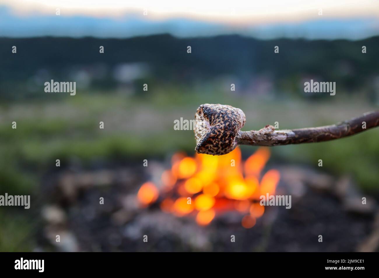 Geringe Schärfentiefe des verbrannten Sumpfes. Süße zuckerhaltige Süßwaren auf einem Stock mit Feuerhintergrund. Stockfoto