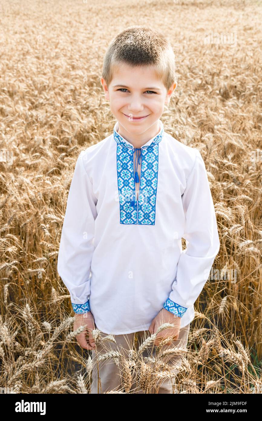 Weiche selektive Fokus des Jungen in traditionellen weißen und blauen bestickten ukrainischen Hemd auf dem Hintergrund des Weizenfeldes an sonnigen Tag. Kind lächelt. Ind Stockfoto
