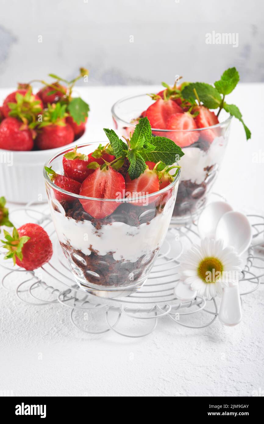 Kleinigkeiten. Brownies, frische Erdbeere und Mascarpone-Creme in Schichten auf Glas auf weißem Hintergrund gezackt. Portionsdesserts. Kein gebackener Brownie Cheesecak Stockfoto