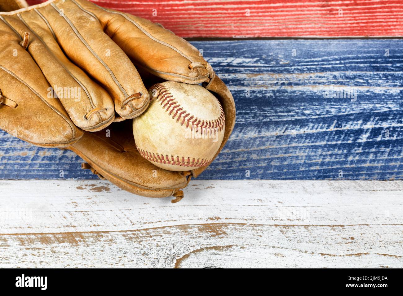 Alt abgenutzter Baseballhandschuh und Ball auf verblassten Brettern, die in amerikanischen Nationalfarben gestrichen sind Stockfoto