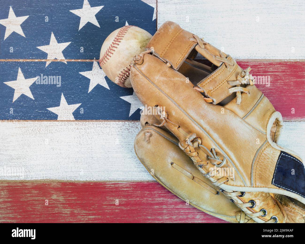 Alt abgenutzter Baseballhandschuh und Ball auf verblassten Brettern, die in amerikanischen Nationalflaggenfarben gestrichen sind Stockfoto