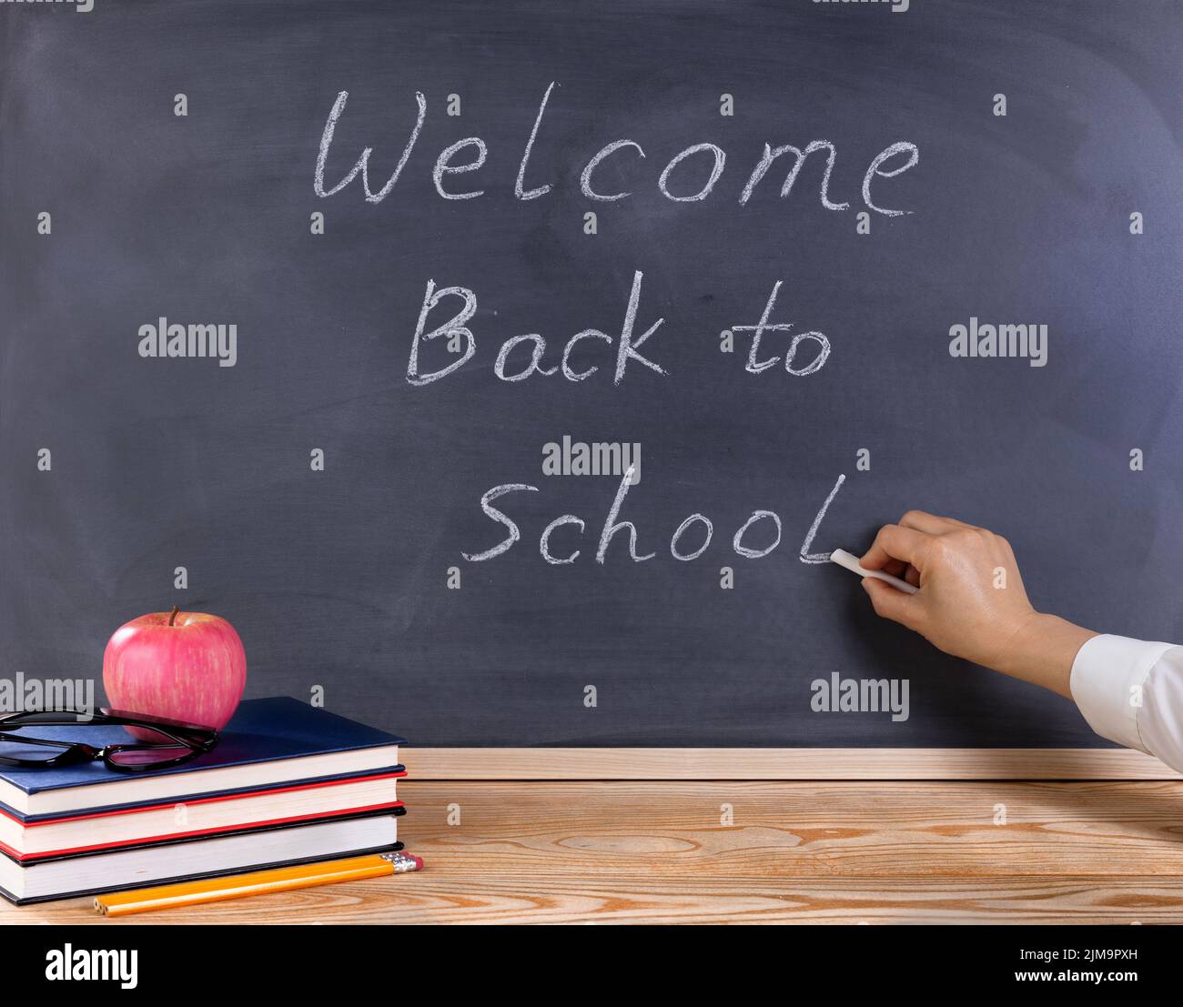 Lehrer schreiben willkommen zurück in der Schule auf gelöscht schwarzen Kreidetafel mit Schreibtisch und Zubehör vor Stockfoto