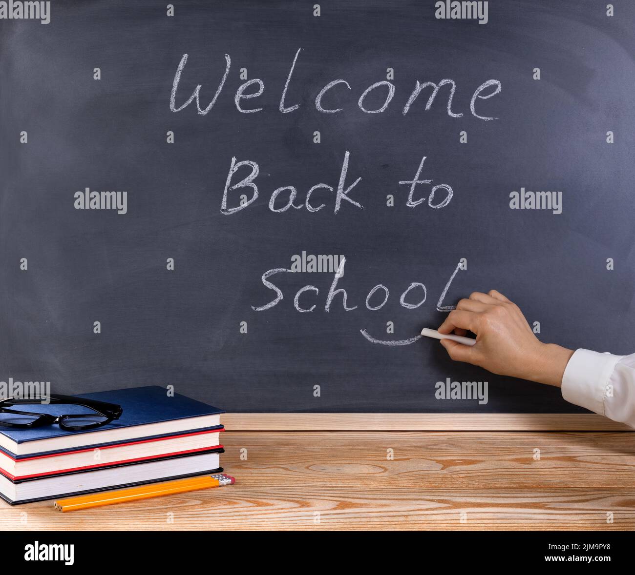 Der Lehrer setzt ein Lächeln-Symbol auf die Nachricht „Willkommen zurück zur Schule“ mit dem Schreibtisch und den Vorräten Stockfoto