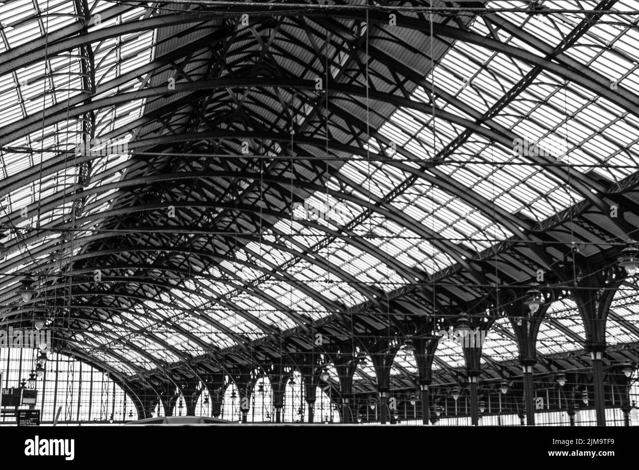 Eine Nahaufnahme des Bahnhofs mit einem geschwungenen Stahldach über dem Dach. England. Graustufenaufnahme Stockfoto