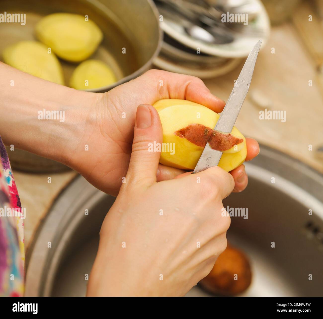 Frau schneidet Kartoffeln, um sie zu schälen. Küche funktioniert. Bereiten Sie das Essen zu Stockfoto