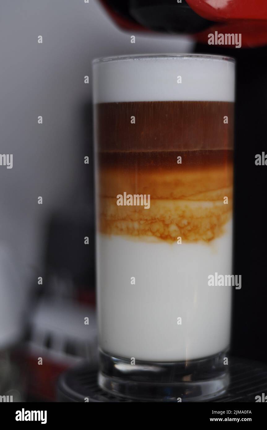 Eine vertikale Nahaufnahme von dreilagiger Latte Macchiato in einem hohen Glas. Stockfoto