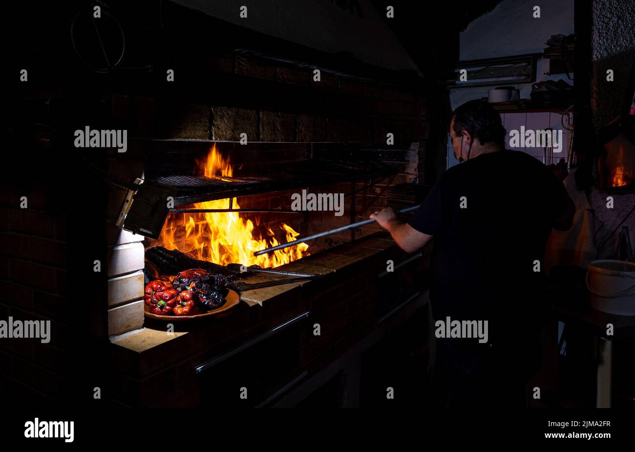 Eine schöne Aufnahme eines Mannes, der neben einem Steinofen steht und mit einer gegrillten Paprika-Platte auf der Seite kocht Stockfoto