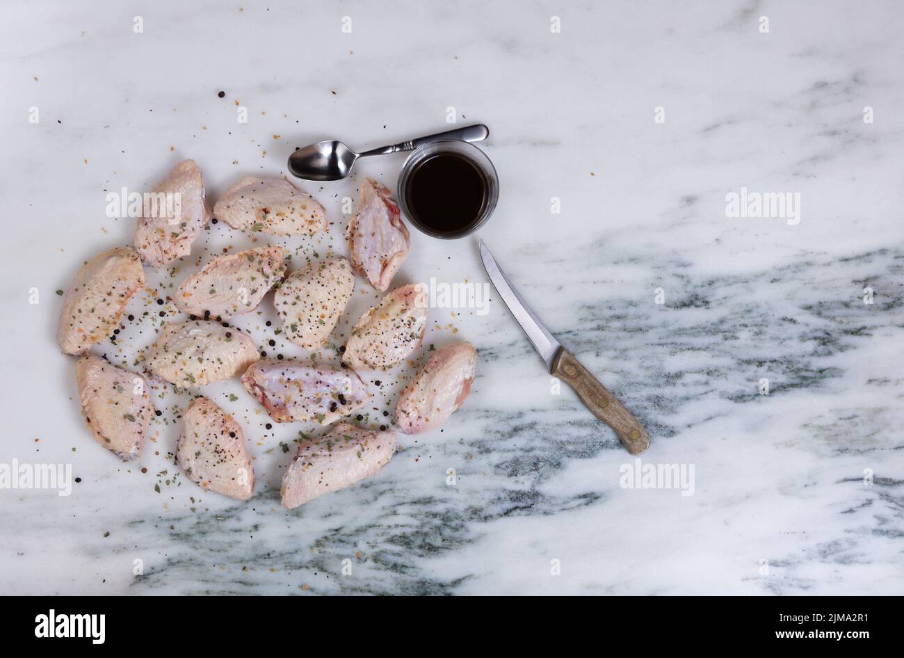 Frische rohe Hähnchenflügel und Kochgewürze auf Marmorstein-Arbeitsplatte Stockfoto