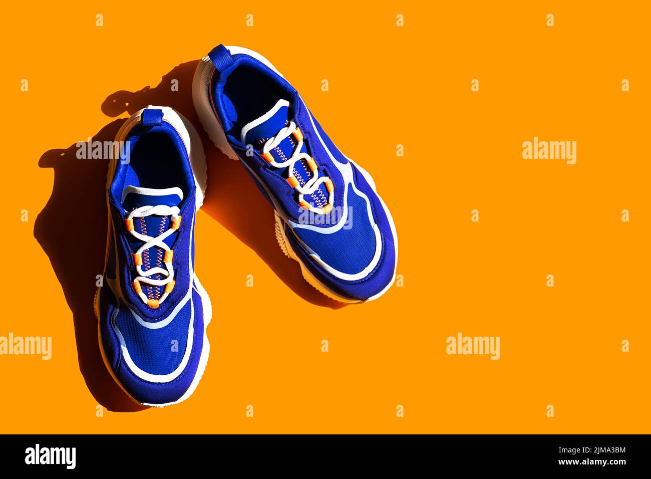Blaue Sneakers auf orangefarbenem Hintergrund. Trendige Sportschuhe, lässige Straßenschuhe. Stockfoto