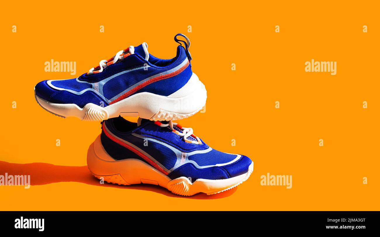 Blaue Sneakers auf orangefarbenem Hintergrund. Trendige Sportschuhe, lässige Straßenschuhe. Stockfoto