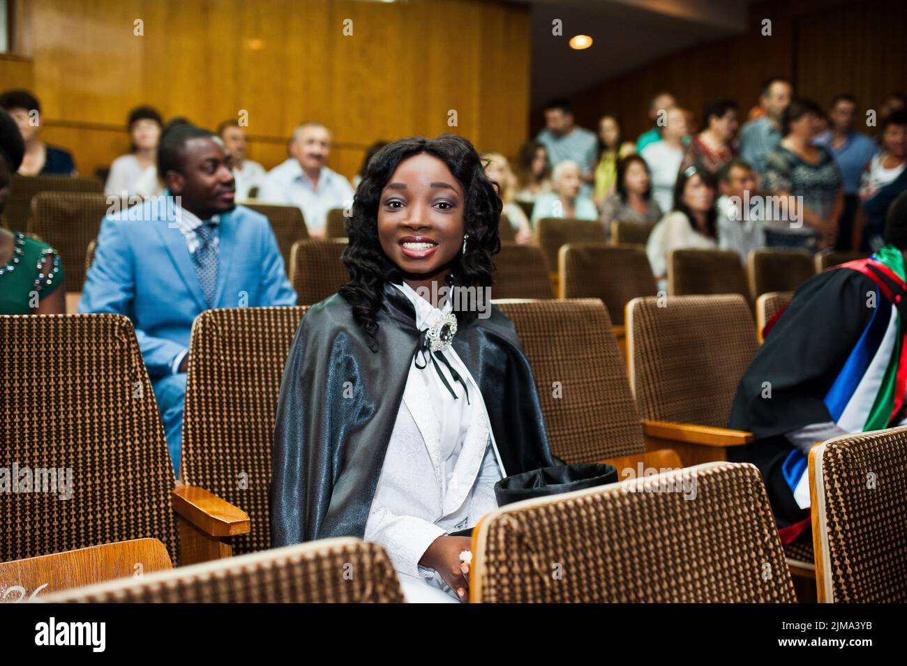 Glückliches schönes schwarze afroamerikanische Mädchen mit Hut und Mantel Absolventen bei Zeremonie Schloss Stockfoto