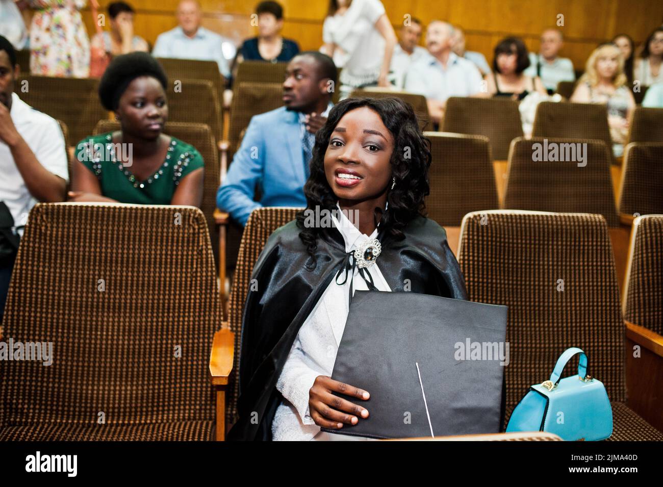 Glückliches schönes schwarze afroamerikanische Mädchen mit Hut und Mantel Absolventen bei Zeremonie Schloss Stockfoto