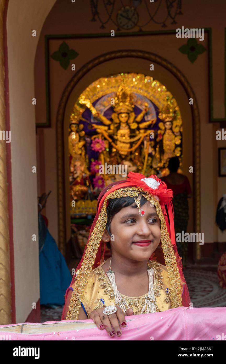 Howrah, Indien -26.. Oktober 2020 : Bengalisches Mädchen in festlichem Kleid, lächelnd und posiert mit Göttin Durga im Hintergrund, im alten Haus. Stockfoto