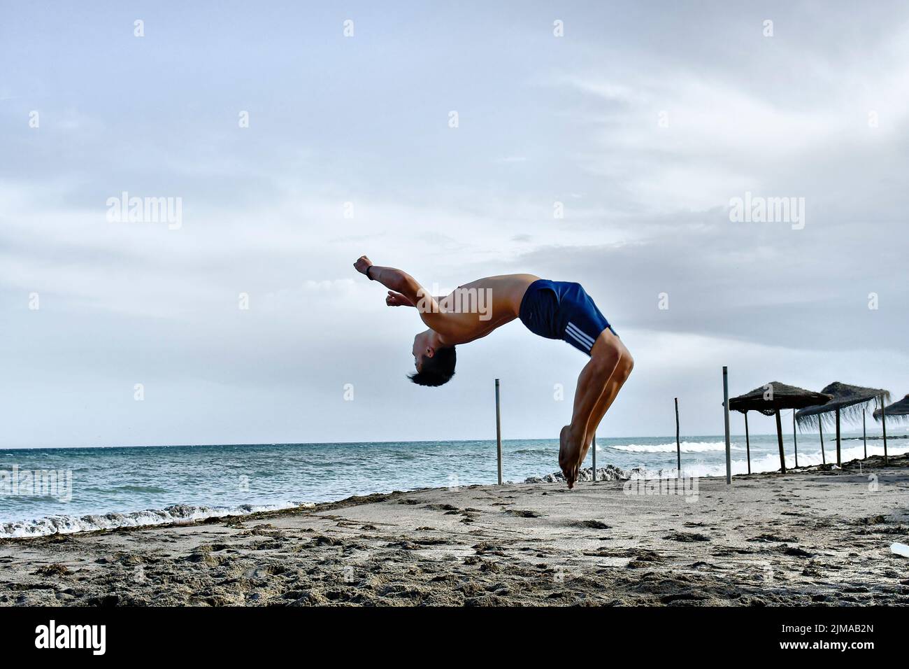 Ein junger Mann, der Backflips macht, wirft Saltos in den Sand. Stockfoto