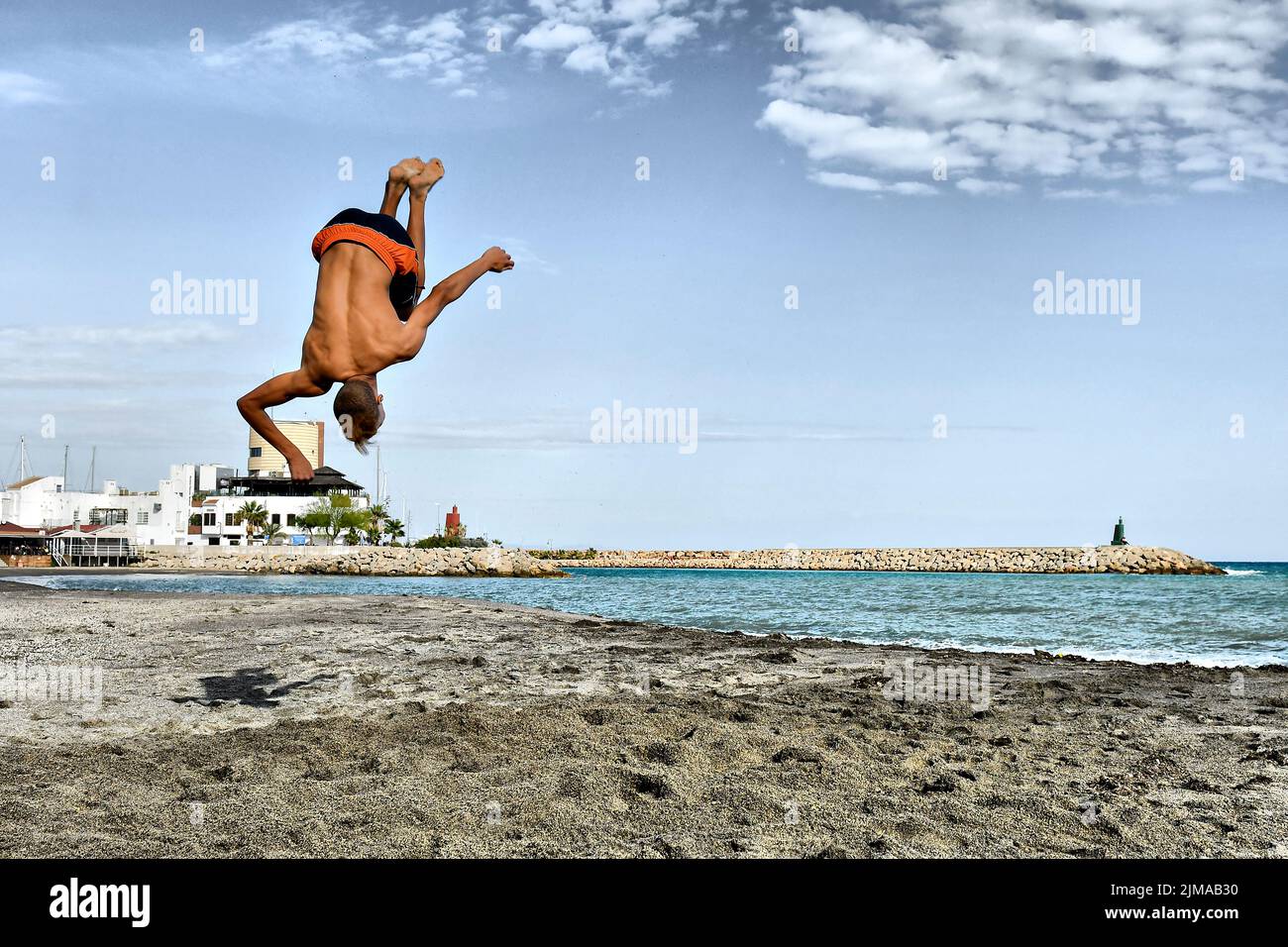 Ein junger Mann, der Backflips macht, wirft Saltos in den Sand. Stockfoto