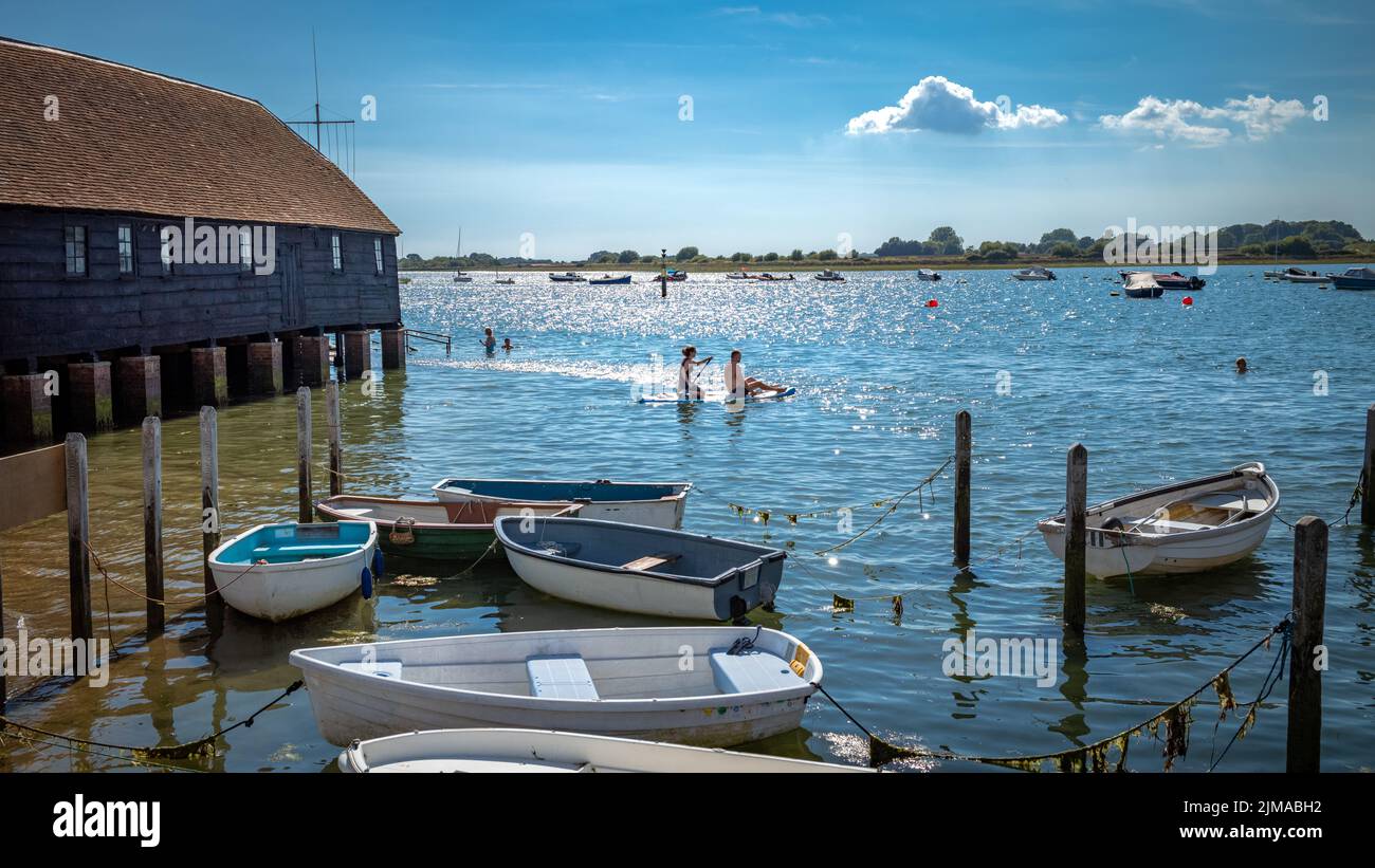 Ein Paar auf einem Paddelbrett schwimmt neben dem Bosham Sailing Club Bootshaus in Bosham, West Sussex, Großbritannien. Stockfoto