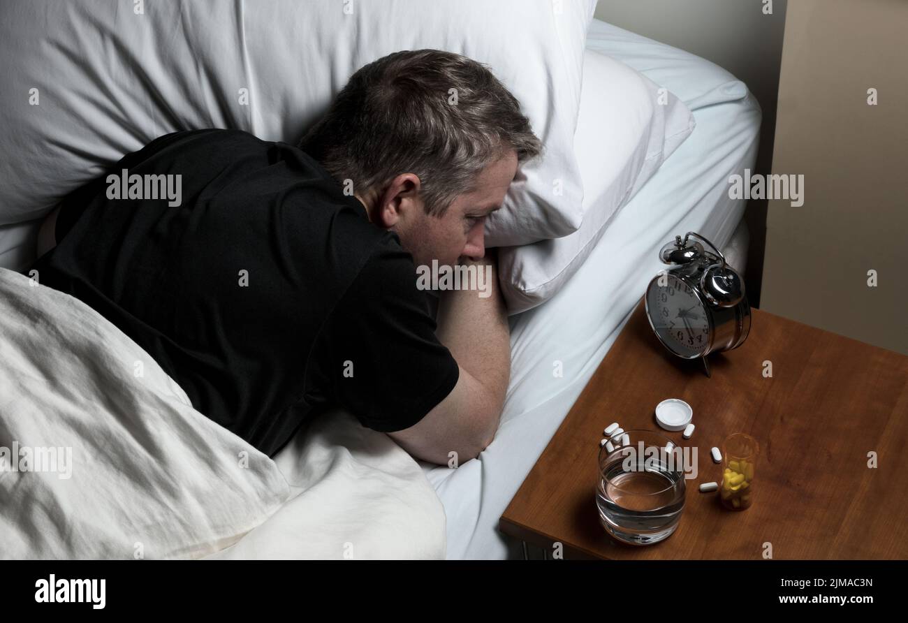 Reifer Mann mit Schwierigkeiten beim Einschlafen in der Nacht, also wach und starrte auf Wecker Stockfoto