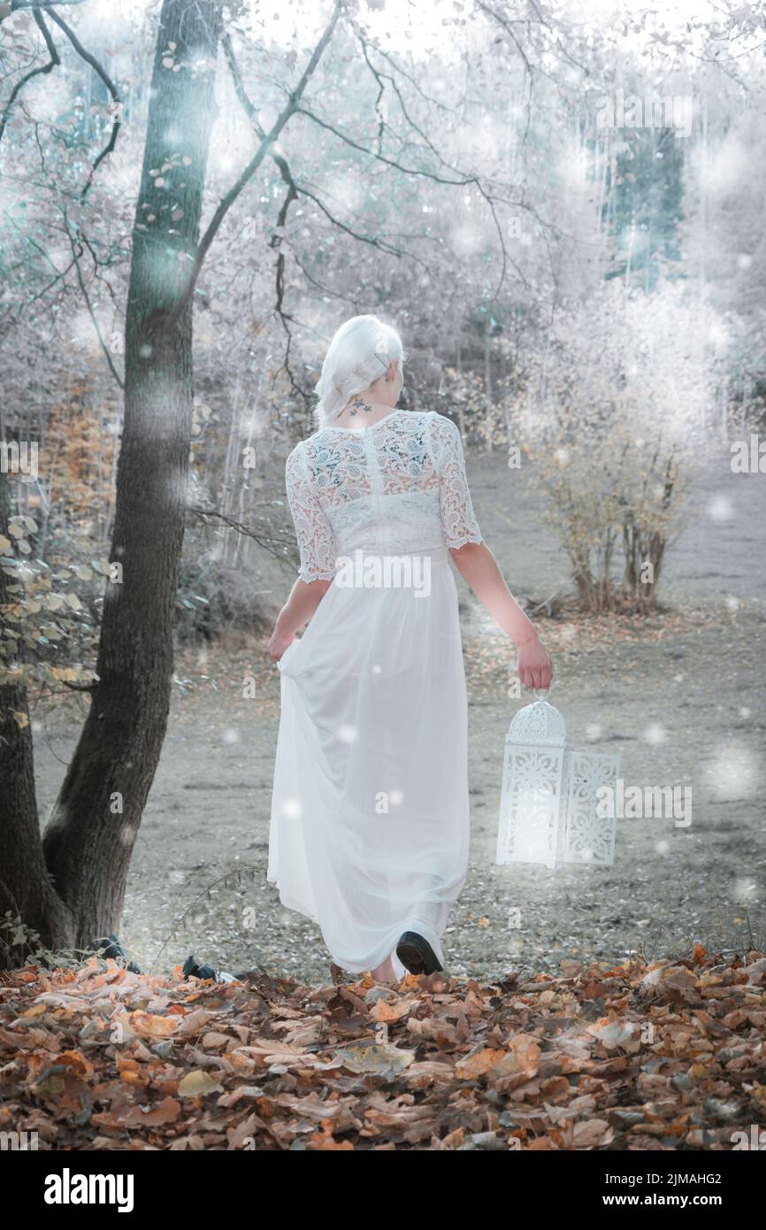 Eine Frau geht mit weißem Kleid und Laterne durch einen Wald Stockfoto