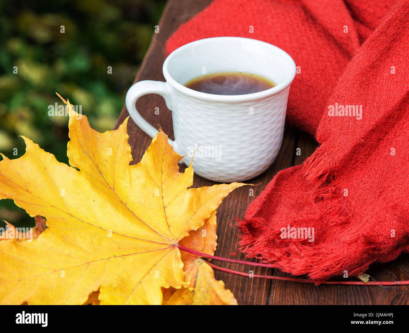 Tasse Tee auf dem Tisch mit einem Schal und gelben Blättern Stockfoto