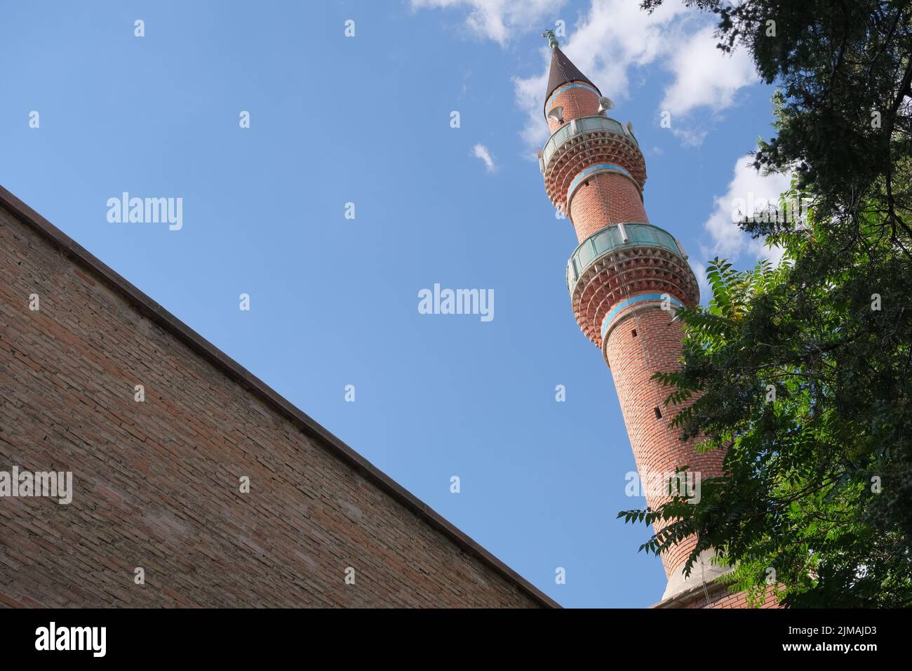 Blick auf Minarett, Eckansicht der Moschee im Zentrum von Konya, Minarett aus roten Ziegeln über grünem Baum. Stockfoto