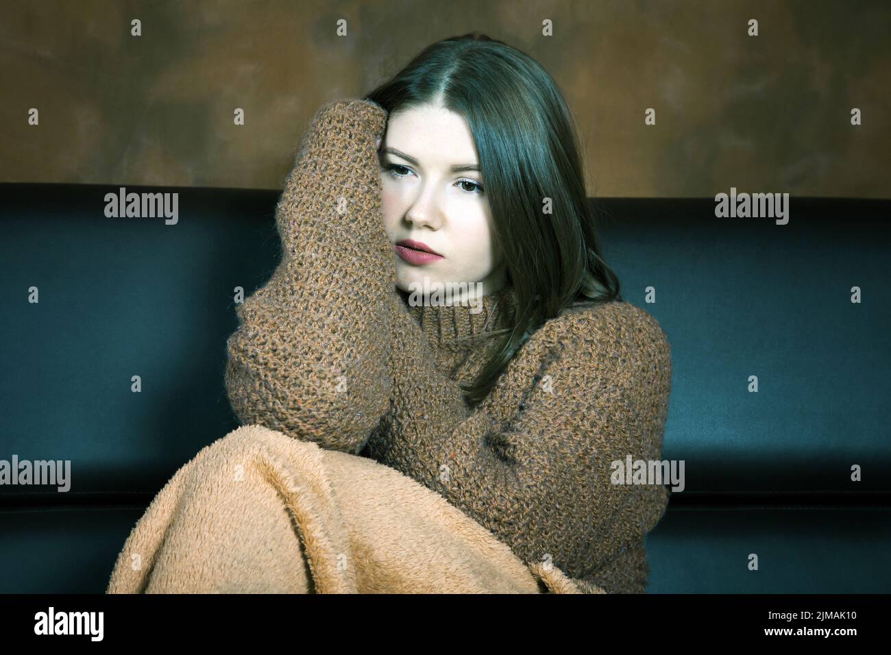 Mädchen in einem Pullover sitzt auf der Couch eingewickelt in einen Teppich Stockfoto