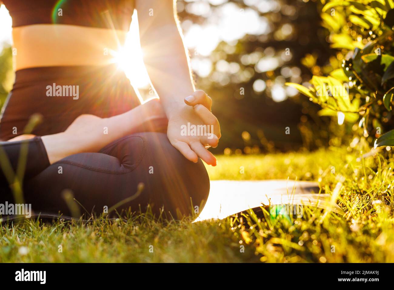 Nahaufnahme des Körpers einer jungen Frau, die in Lotushaltung sitzt, atmet und meditiert. Konzept von Outdoor Yoga, Entspannung, Zen und mentaler Balance. Wunderschön Stockfoto