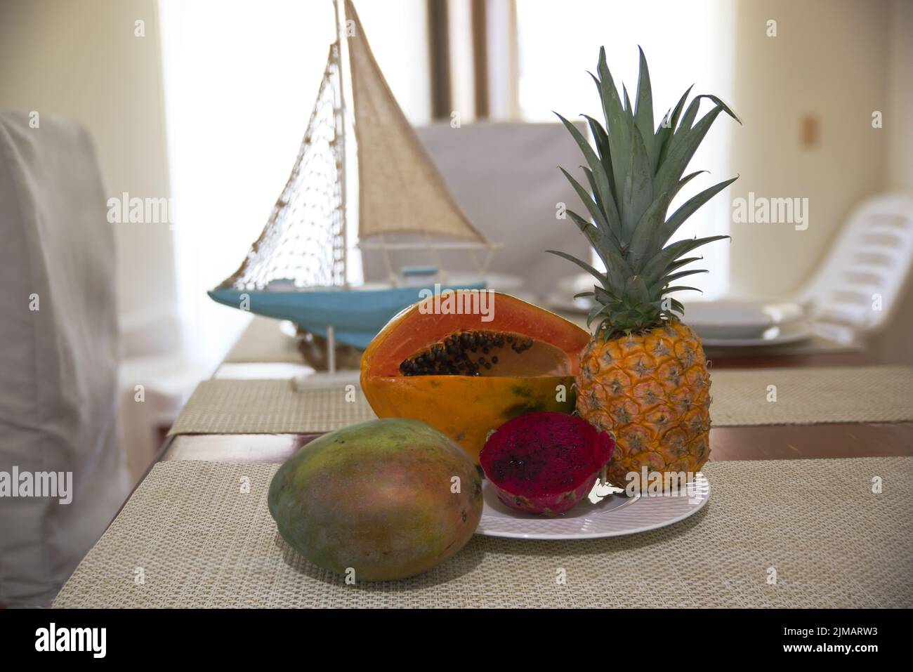 Exotische Früchte auf dem Tisch mit Servietten, Yachtmodell und Fenster Stockfoto
