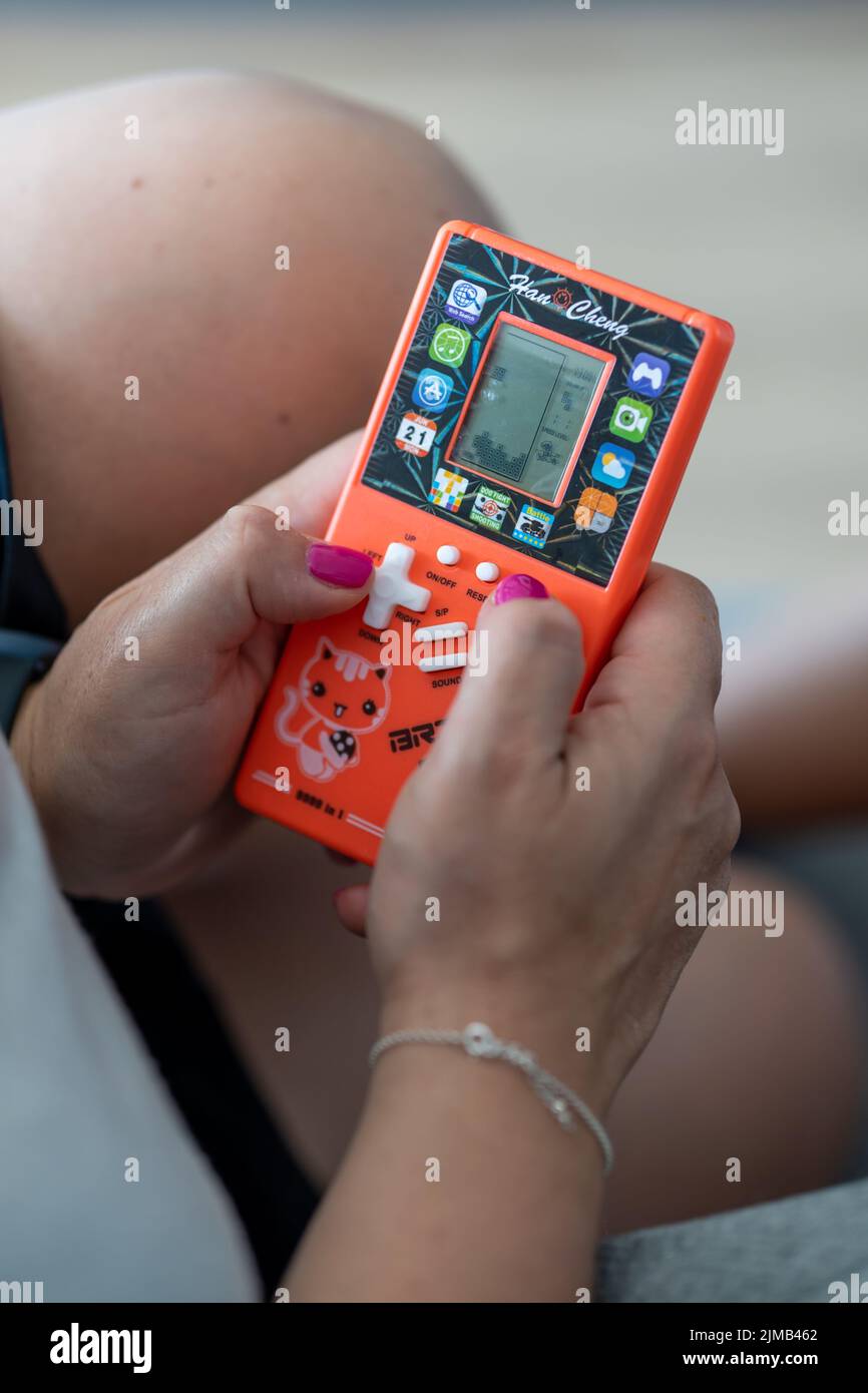 Eine vertikale Nahaufnahme einer Frau, die ein Backsteinspiel mit einer orangefarbenen Han Cheng Handkonsole spielt Stockfoto