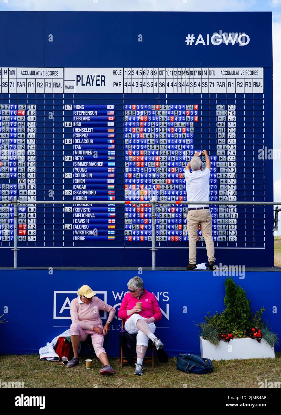Gullane, Schottland, Großbritannien. 5.. August 2022. Zweite Runde der AIG Women’s Open Golf Championship in Muirfield in East Lothian. Bild; zwei Zuschauer machen eine Pause unter der großen Anzeigetafel im Zuschauerdorf. Iain Masterton/Alamy Live News Stockfoto
