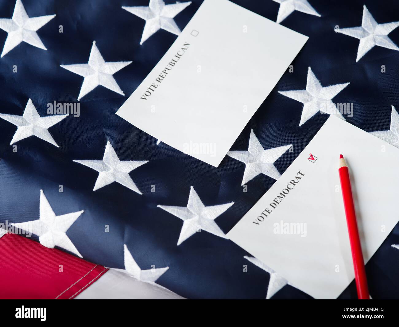 Vor dem Hintergrund der amerikanischen Staatsflagge, zwei Zettel mit einem Aufruf, für Republikaner oder Demokraten zu stimmen, ein roter Bleistift. Parlamentarische E-Fraktion Stockfoto