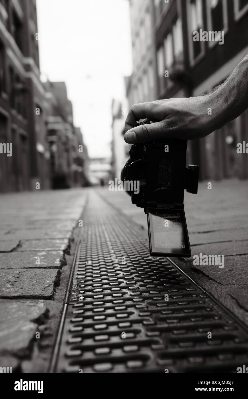 Eine vertikale, Graustufenaufnahme einer Hand, die die Kamera sehr nah über dem Boden hält, kann für Fotokursanzeigen verwendet werden Stockfoto