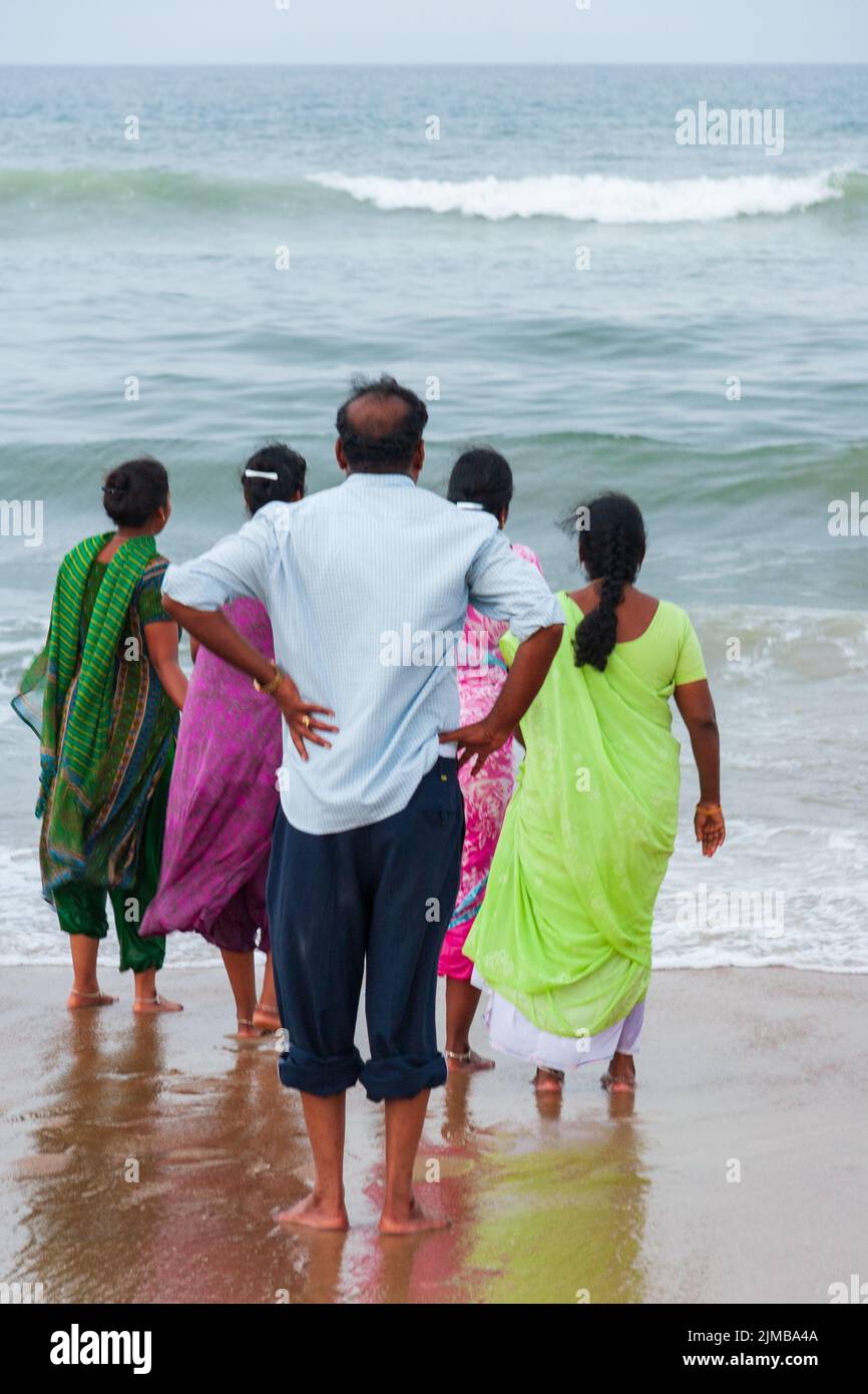 Ein Mann und vier Frauen blicken barfuß auf das raue Meer am beliebten Marina Beach in Chennai Stockfoto
